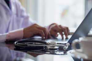 Clinical employee working on laptop with stethoscope on desk 