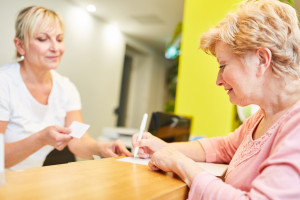 White elderly woman in pink shirt at healthcare registration desk