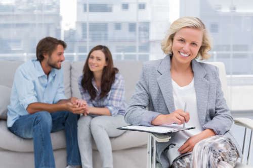 Blonde female therapist sitting at desk and young couple sitting on couch